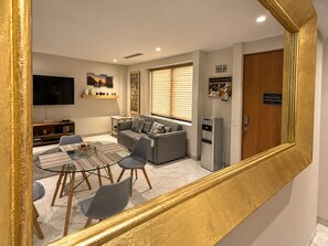 A living room with a sofa, a coffee table, and a TV. There is a door with a sign on it and a refrigerator.
