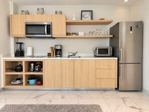A modern kitchen with wooden cabinets, a stainless steel refrigerator, a microwave, a coffee maker, and a toaster.