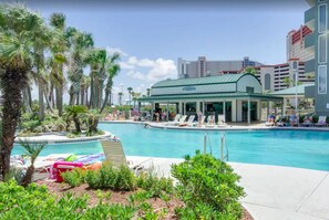 A hotel with a pool area, surrounded by palm trees and a covered seating area.