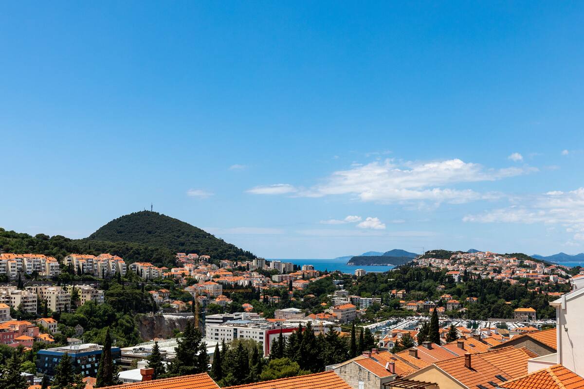 Un paysage urbain côtier avec de nombreux immeubles résidentiels, une colline imposante surmontée d’un monument et un ciel bleu dégagé.