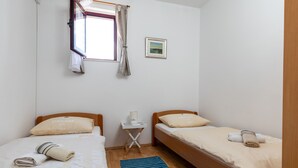 A small, clean room with two beds, a window with curtains, a bedside table with a lamp, and a framed picture on the wall. - Apartments Franka (Dubrovnik)