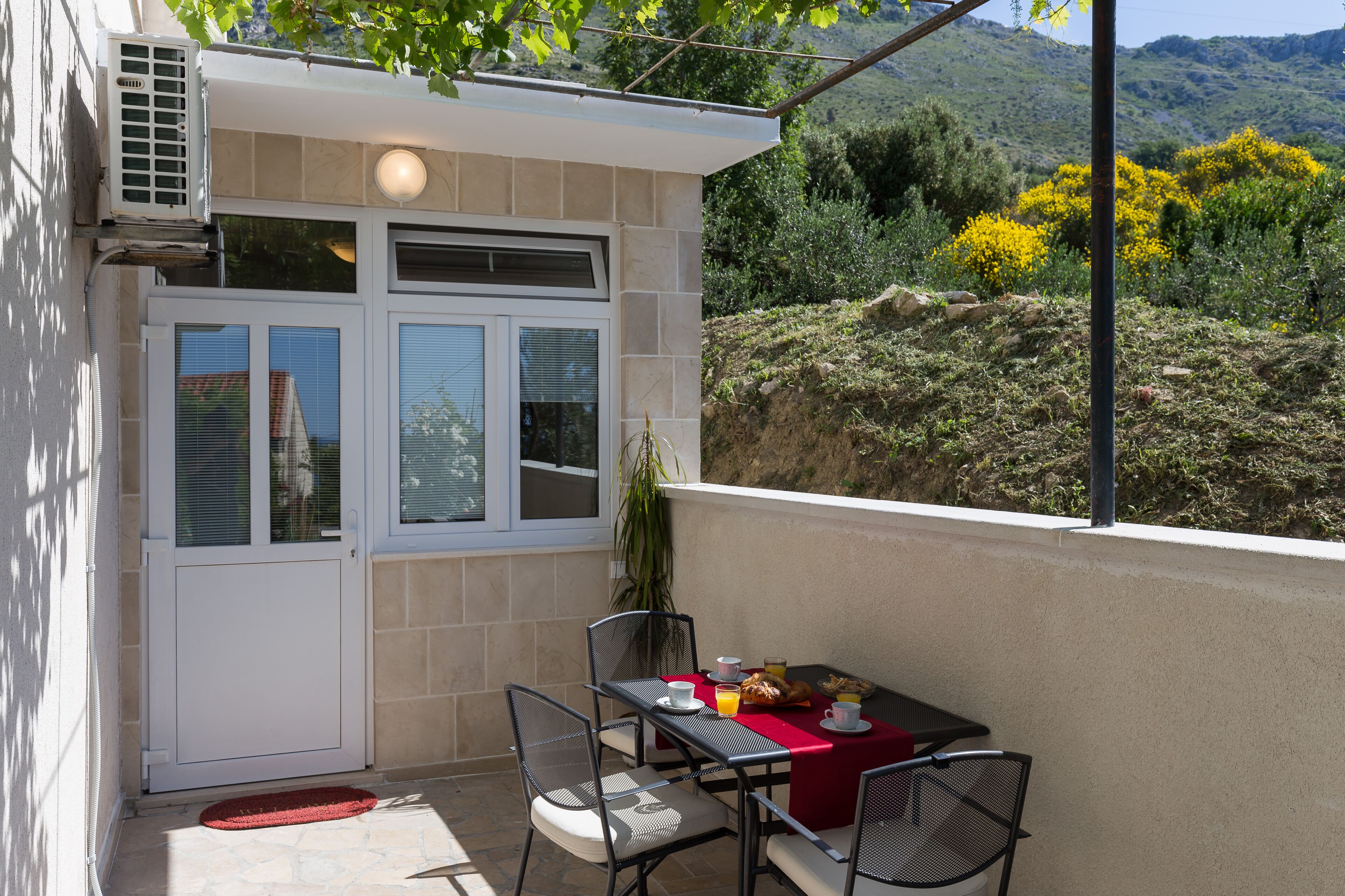 Un petit espace extérieur aménagé pour prendre les repas, avec une table, des chaises et une nappe rouge.