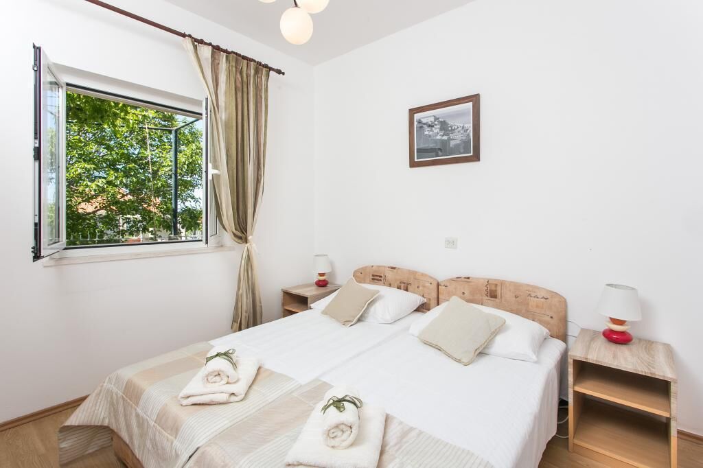 A bedroom with a large bed, two bedside tables, a window with curtains, and a framed picture on the wall.