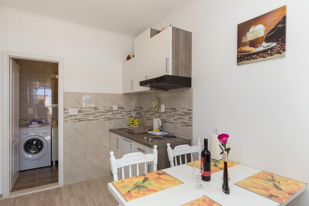 A compact kitchen with a washing machine, a dining area with a table and chairs, and a painting on the wall.