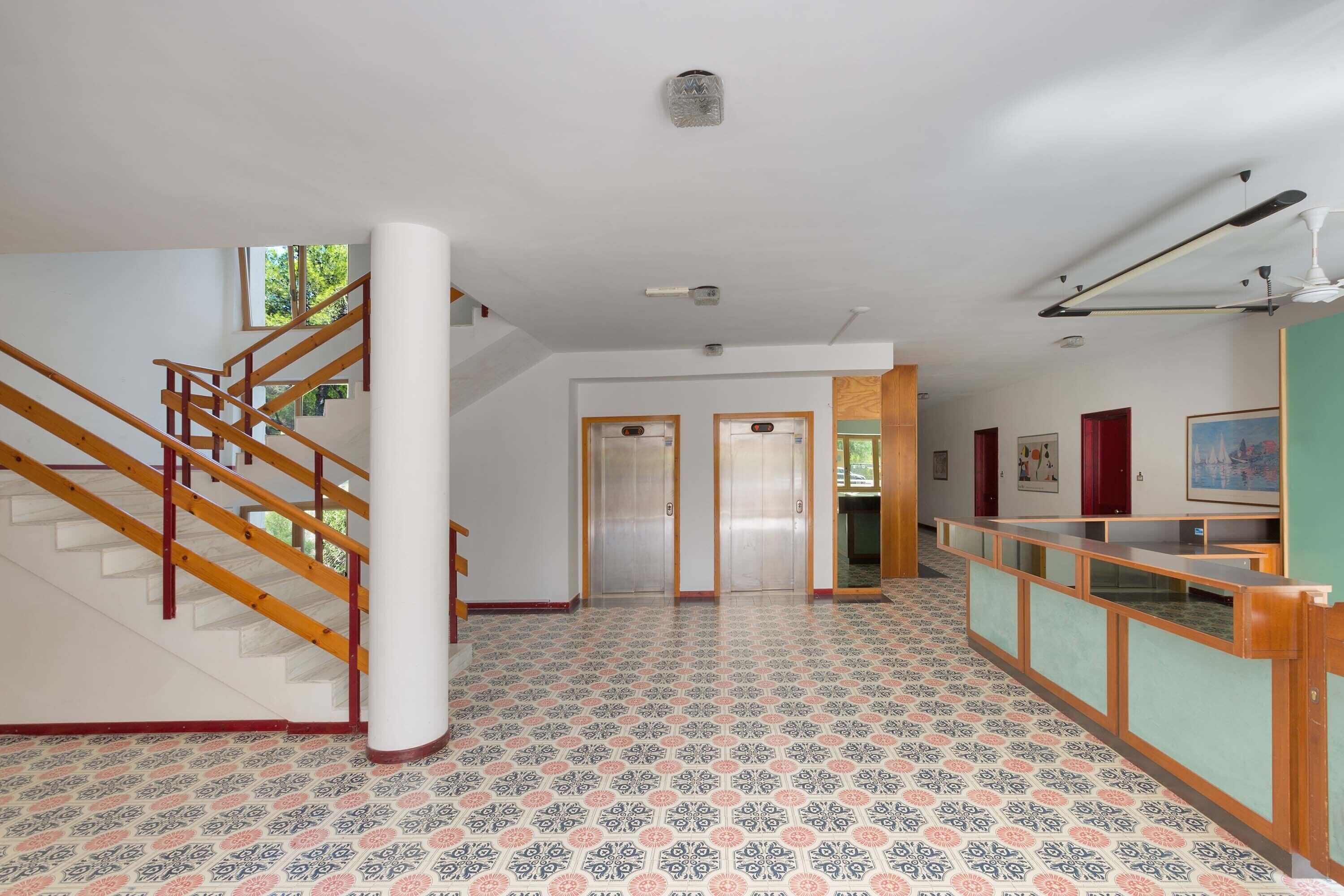 Eine geräumige Lobby mit gemustertem Boden, einer Holztreppe und einem Empfangsschalter.