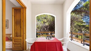 A balcony with a red tablecloth, white chairs, and a view of trees through an archway. - 2507 Red Apartment by Barbarhouse (Vernole)