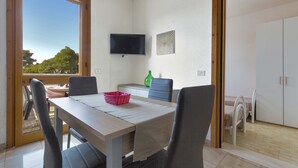 A dining area with a table, chairs, a TV, and a view through a window. - 2728 Villetta Chiara Blu Primo Piano by Barbarhouse (Melendugno)