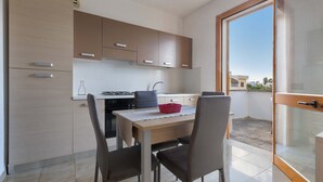 A modern kitchen with a dining area, featuring a table with chairs, a red basket, and a view through a glass door to the outside. - 2728 Villetta Chiara Blu Primo Piano by Barbarhouse (Melendugno)