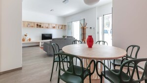 A modern living room with a round wooden table, green chairs, a grey sofa, and a red vase. - 2488 Villa Gaia by Perle di Puglia (Cavallino)