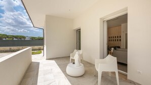 A modern, minimalist balcony with white chairs and a decorative sculpture, leading to a living area with a sofa and a coffee table. - 2488 Villa Gaia by Perle di Puglia (Cavallino)