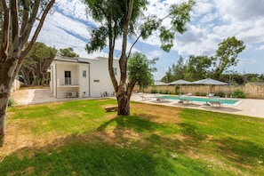A backyard with a swimming pool, a white house, and a large tree. - 2488 Villa Gaia by Perle di Puglia (Cavallino)