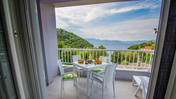 Varanda com uma mesa posta para dois, com vista panorâmica para colinas e um corpo d'água.