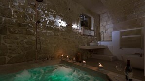 A stone-walled bathroom with a bathtub, candles, and a wine bottle. - 2661 Porta del Duomo Luxury by Barbarhouse (Lecce)