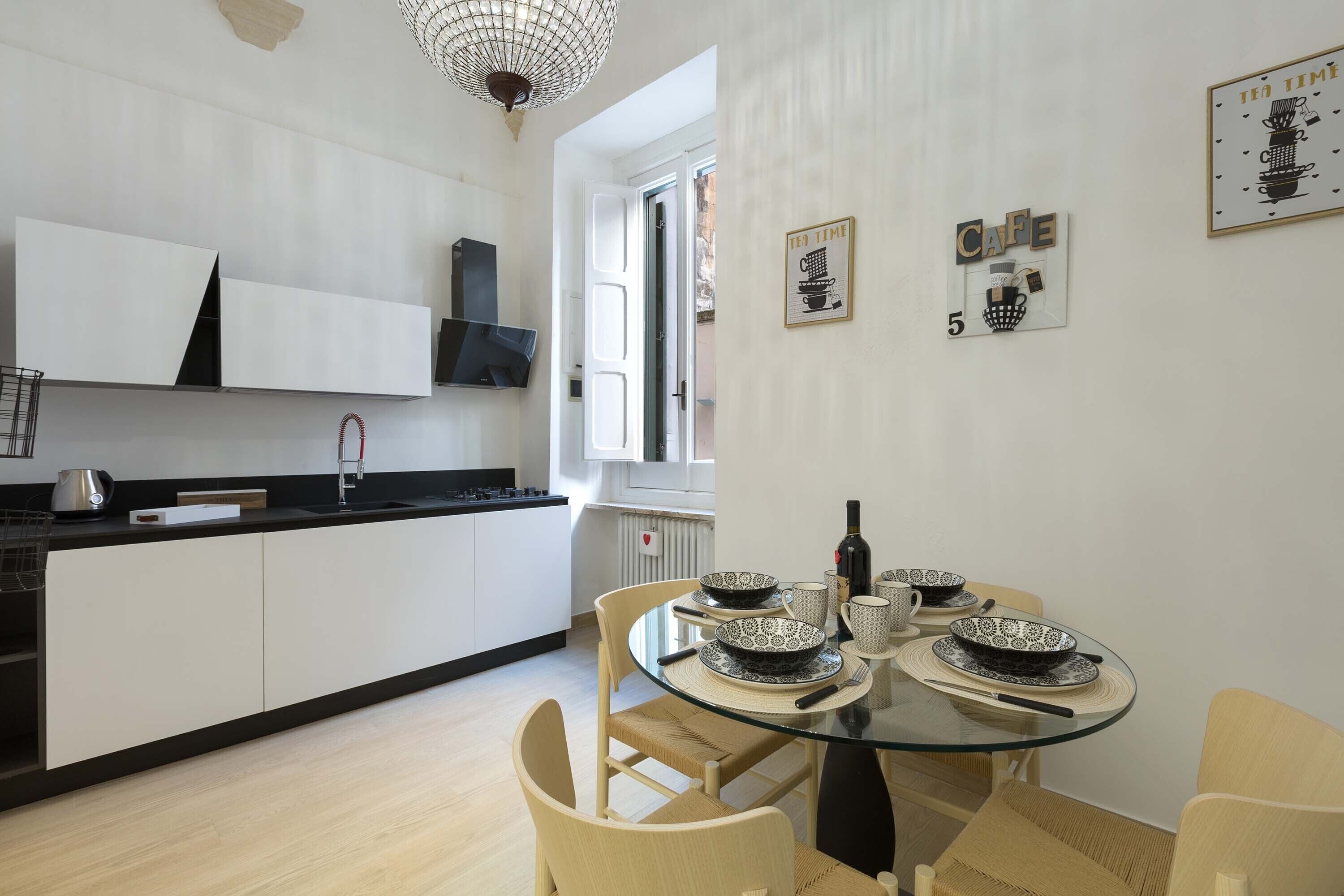 Une cuisine moderne avec des meubles blancs, une table à manger en verre et une fenêtre offrant une belle vue.