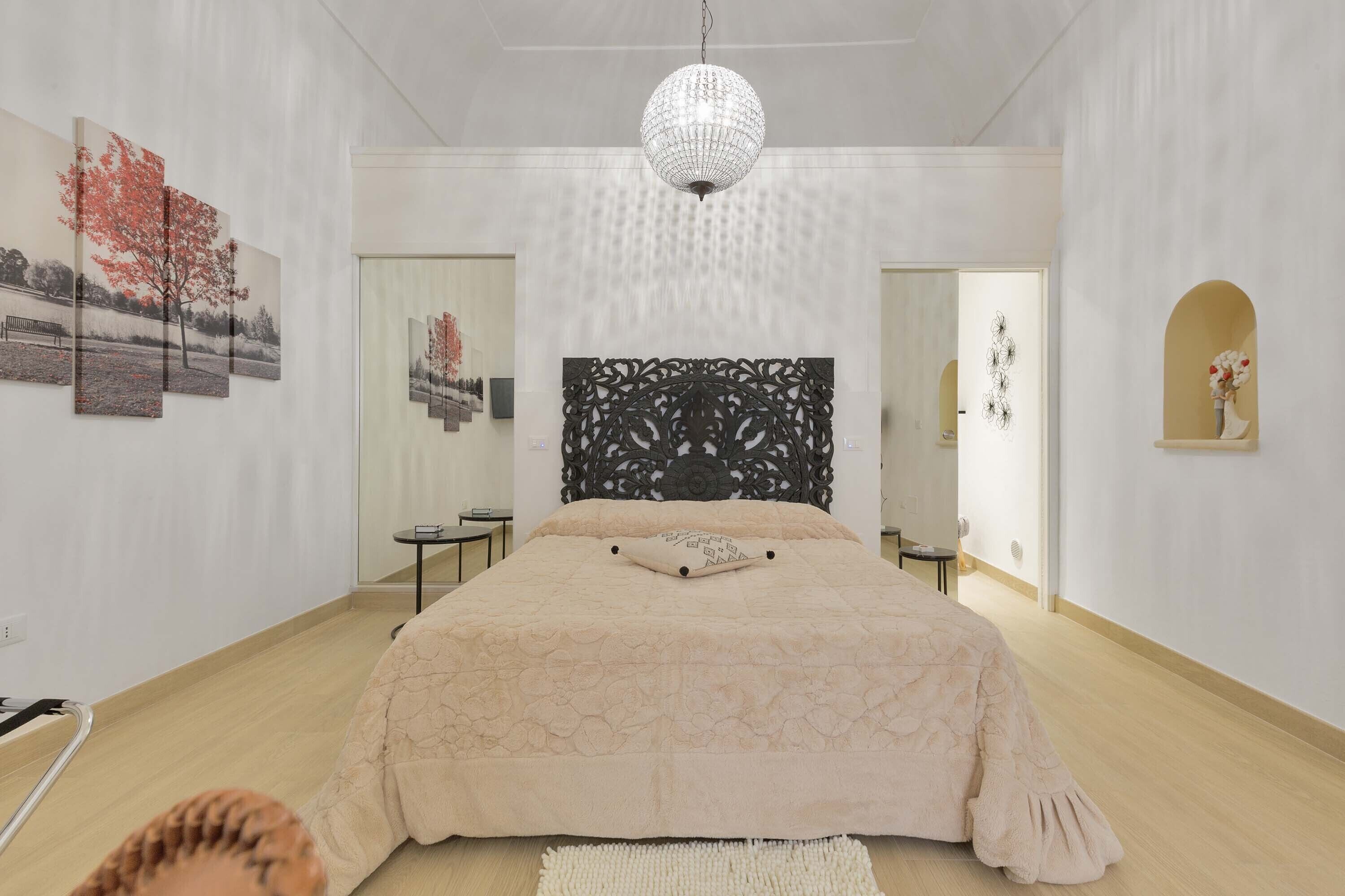 Quarto moderno com cama grande, cabeceira decorativa e lustre.