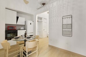 Una cocina moderna con armarios blancos, un microondas rojo y un comedor con mesa y sillas de vidrio.