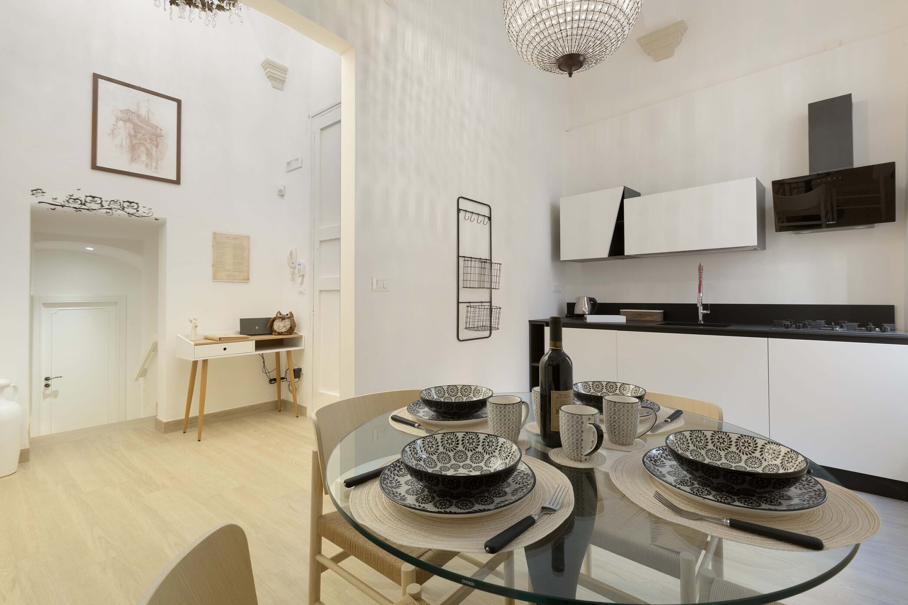 A modern kitchen with white cabinets, a black countertop, and a hanging light fixture.
