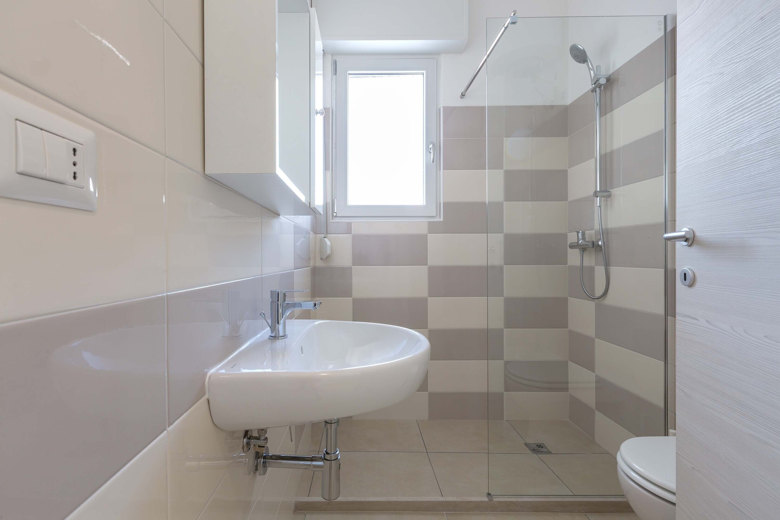 A modern bathroom with a white sink, a glass shower enclosure, and a toilet.