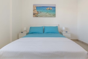A neatly made bed with a white and blue bedspread, two matching pillows, and two bedside lamps on white nightstands.