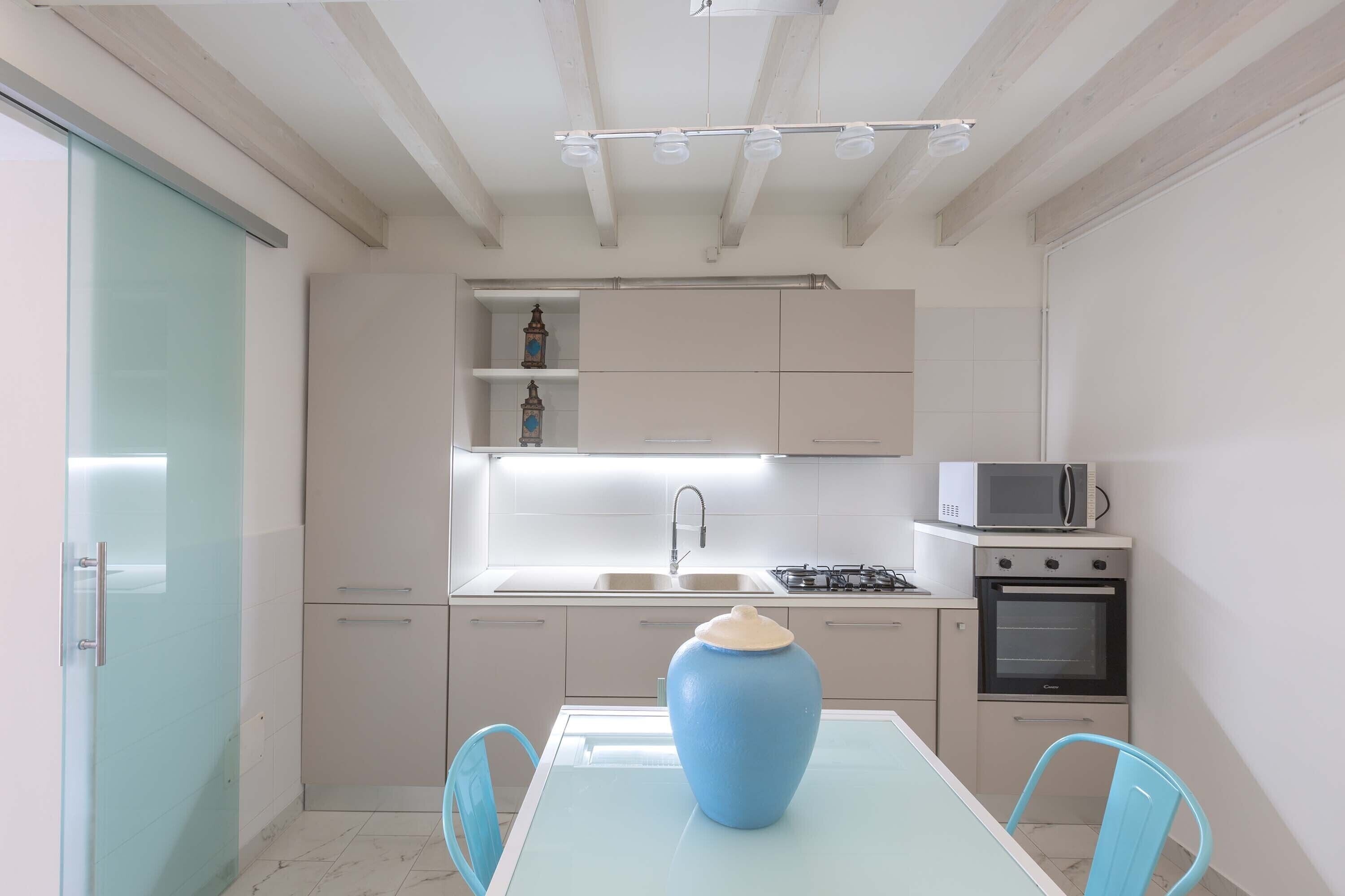 A modern kitchen with white cabinets, a microwave, stove, and a blue vase on the table.