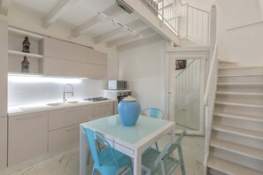 Una cocina moderna con armarios blancos, un jarrón azul sobre la mesa, y una escalera que sube a un nivel superior.