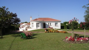 A white house with a red-tiled roof, surrounded by a well-maintained lawn and colorful flower beds. - Chez Bernadou (Machecoul-Saint-Même)