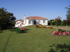 Uma casa branca com telhado de telhas vermelhas, rodeada por um jardim bem cuidado e canteiros de flores coloridos.