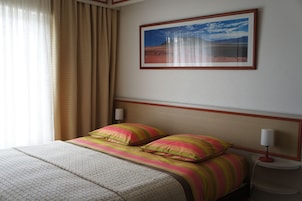 Quarto de hotel com cama, mesa de cabeceira, abajur e um quadro na parede.