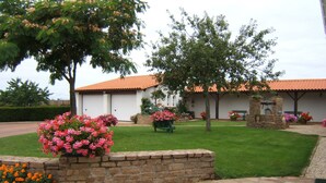 A house with a red-tiled roof, a stone pathway, and various flowering plants. - Chez Bernadou (Machecoul-Saint-Même)