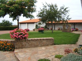 Uma casa com telhado de telhas vermelhas, um caminho de pedra e diversas plantas floridas.