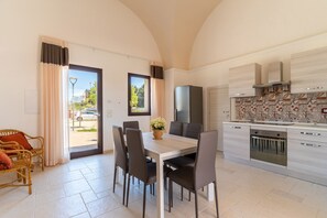 Cozinha moderna com forno embutido, sala de jantar com mesa e cadeiras, e vista pela porta de vidro.