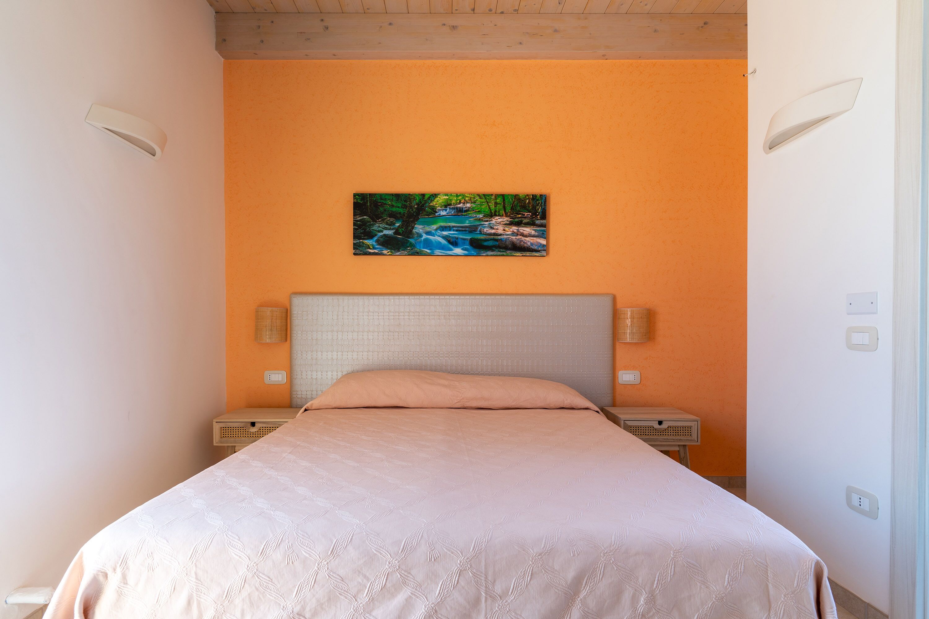Un dormitorio con una cama, un cuadro de un río y una mesita de noche.