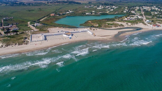 Eine Vogelperspektive einer Küstenregion mit Strand, einem großen Gewässer und einer kleinen Stadt mit Häusern und Gebäuden.