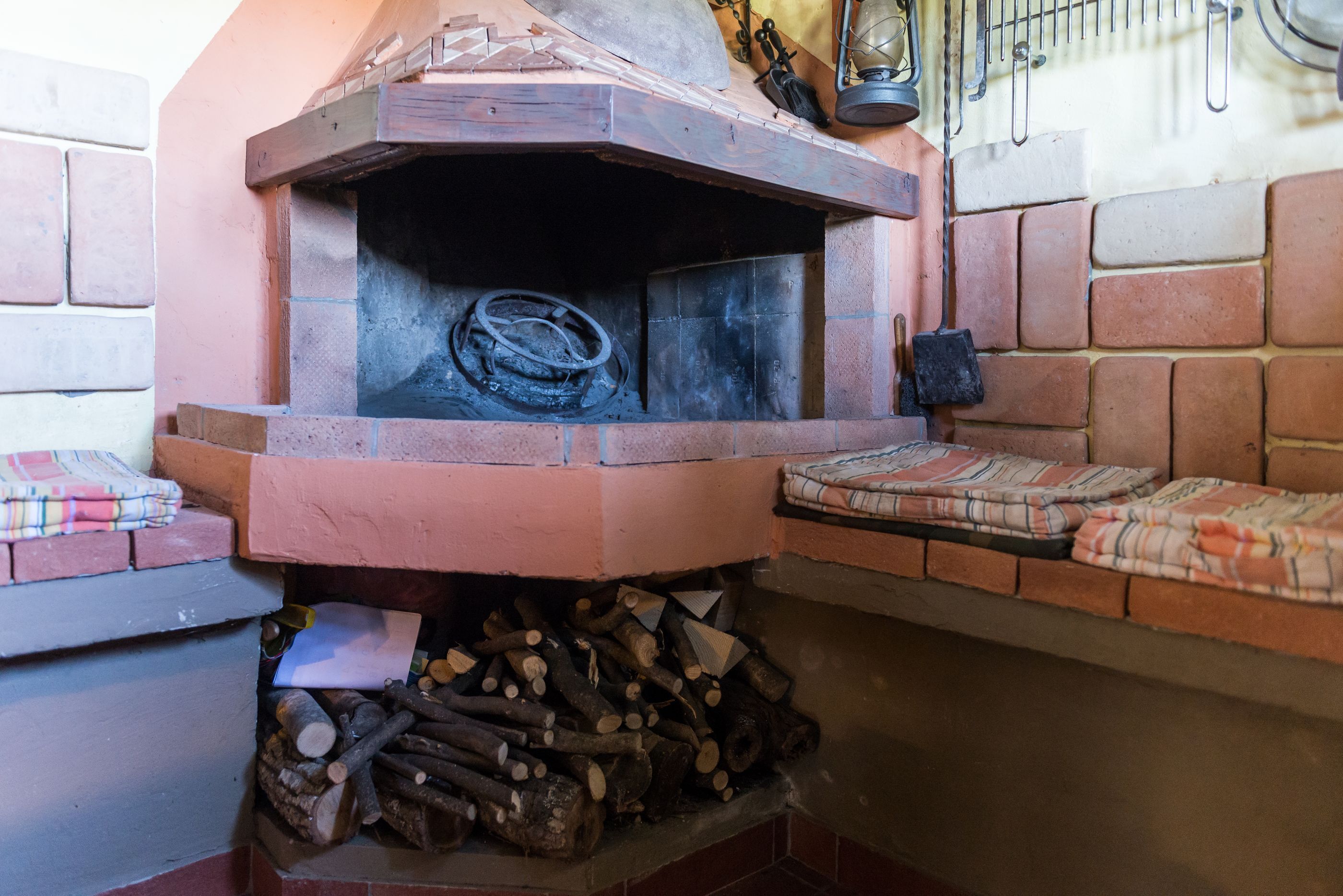 A brick fireplace with a fire, logs, and a lantern.