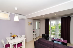 A modern living room with a dining area, a sofa, and a table set with fruits and cups.