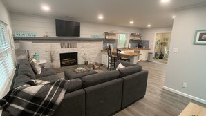 A modern living room with a fireplace, a kitchen in the background, and a dining area. - Restful River House-private dock- on a golf course-5 mins to downtown Kilmarnock (Kilmarnock)