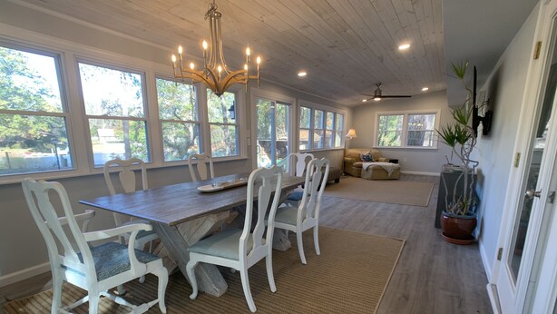 A spacious dining area with a wooden table and white chairs, large windows, and a ceiling fan. - Restful River House-private dock- on a golf course-5 mins to downtown Kilmarnock (Kilmarnock)