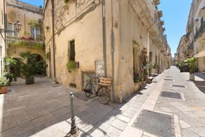 A narrow street with buildings on both sides, a bicycle parked against a wall, and potted plants along the sidewalk.