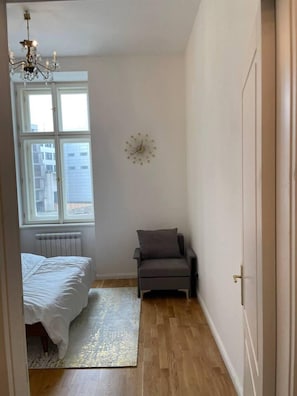 A bedroom with a bed, a chair, a clock, and a window. - 2-bed Apartment in Praha (Prague)