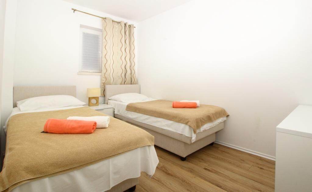 A hotel room with two beds, a nightstand, a lamp, and a window with curtains.