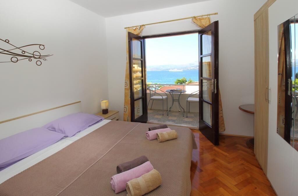 Een slaapkamer met een bed, een klein tafeltje en uitzicht op zee door een open deur.