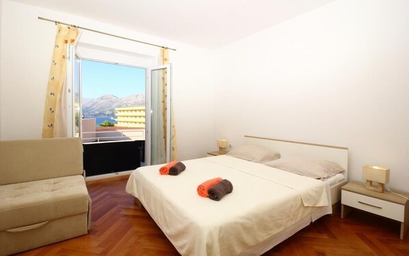 A hotel room with a bed, a chair, a nightstand, and a window with a view of mountains. - Apartments Dubreta (Konavle)