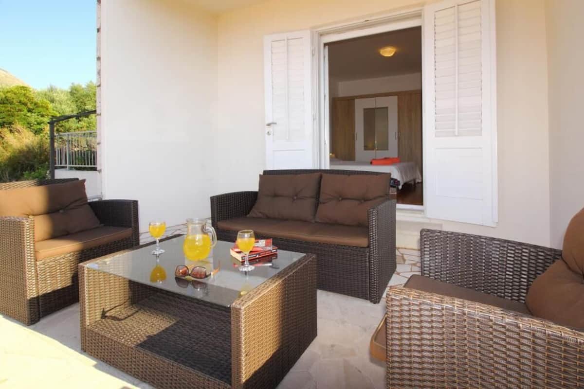 A patio area with wicker furniture, a glass table, and a door leading to an interior space.