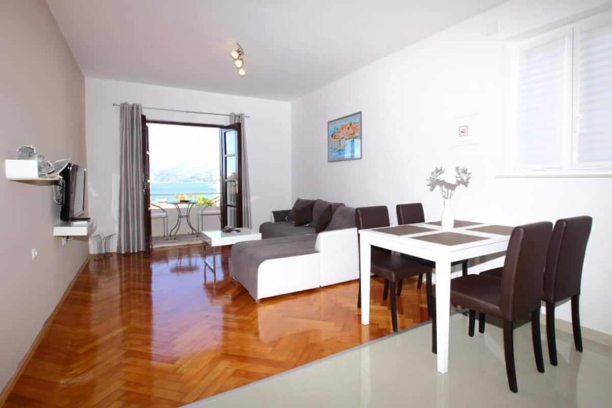 A modern living room with a sofa, dining table, and chairs. There is a window with a view of the outdoors.