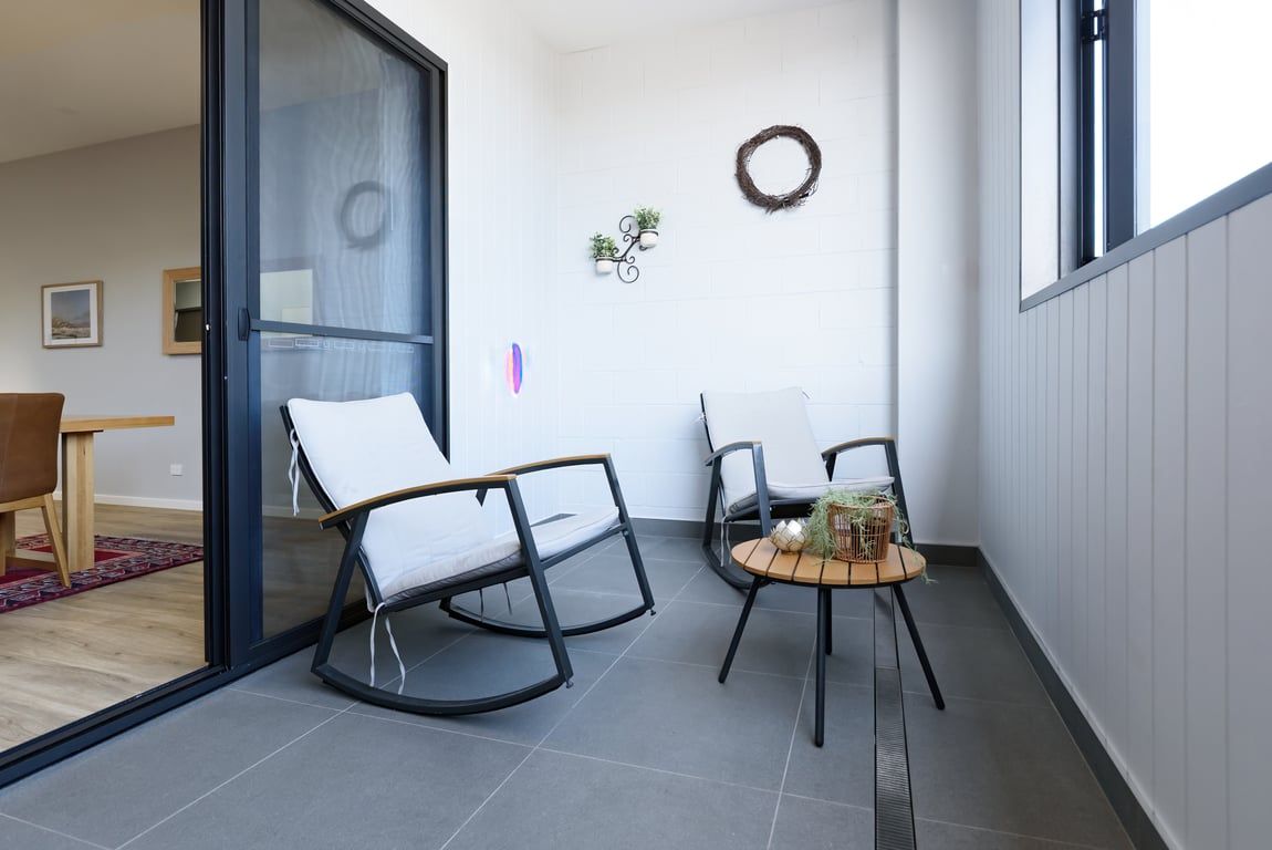Un balcon avec deux fauteuils à bascule, une petite table ornée d’une plante et une vue sur l’intérieur.