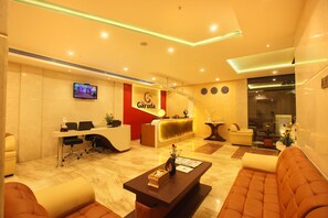 A hotel reception area with a reception desk, seating area, and a television screen.