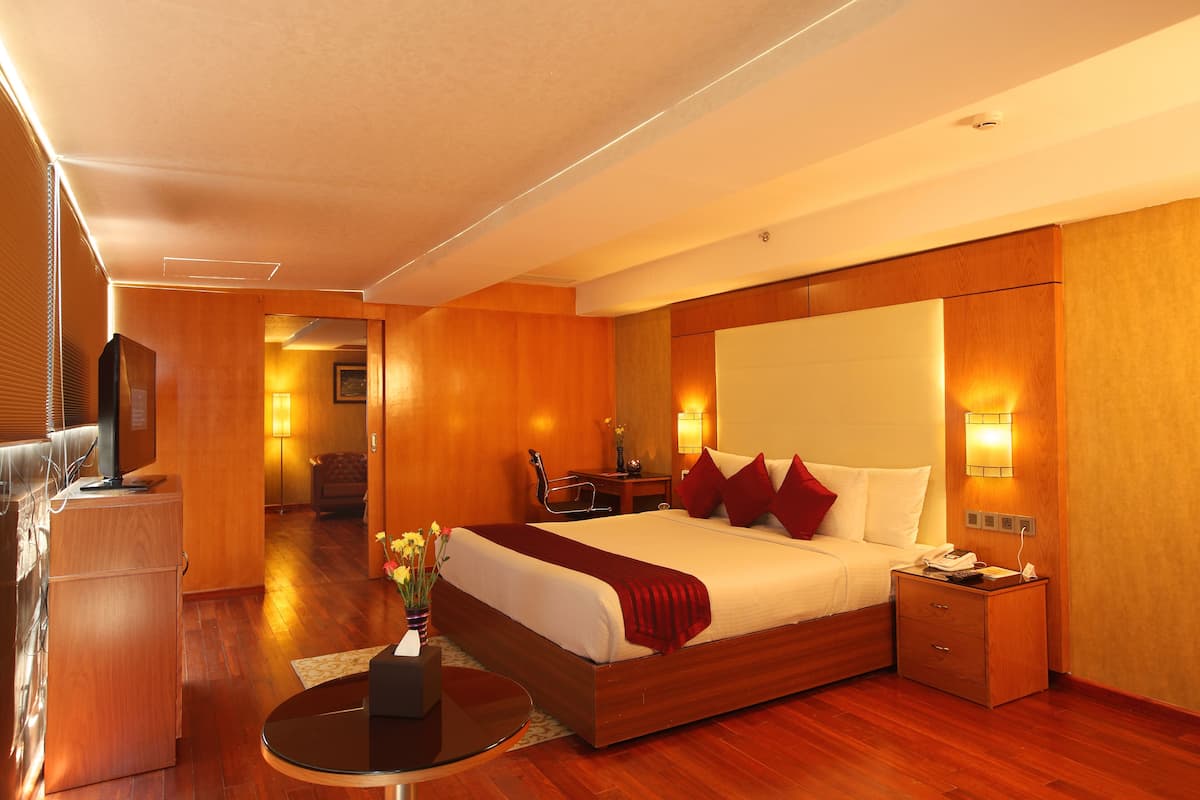 A hotel room with a large bed, bedside table, lamp, and a desk with a chair.