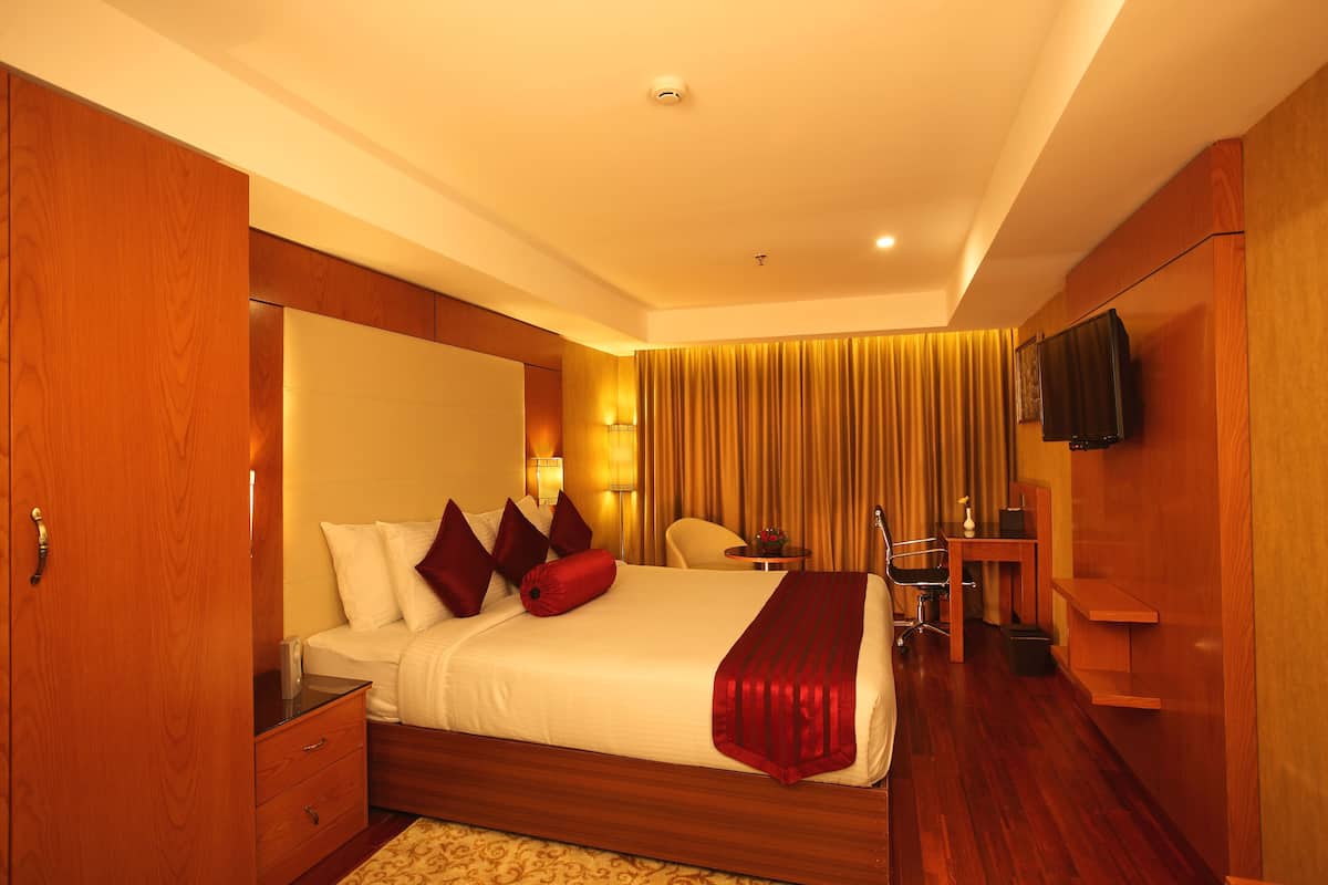 A hotel room with a large bed, wooden wardrobe, bedside table, and a desk with a chair.