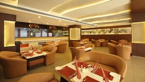 A modern restaurant interior with leather seating, tables set with white tablecloths, and ambient lighting. - The Garuda Hotels (Thrissur)