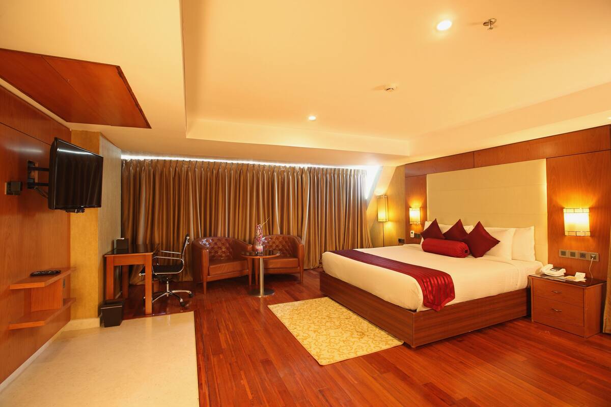 A hotel room with a large bed, a desk, a chair, a TV, and a window with curtains.